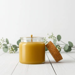 Blossom & Hive 12 hour Beeswax candle in a glass jar with a cork lid placed on a white surface with greenery in the background