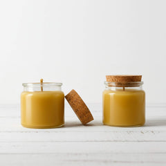 Two Blossom & Hive glass jars with cork lids containing a yellow beeswax candle on a white background