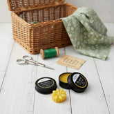 Blossom & Hive Beeswax thread waxes sitting on a white painted timber surface, behind is a wicker basket, green thread spool, and embroidery scissors.
