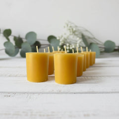 Blossom & Hive 12 beeswax votive refills lined up in a row, on a white wooden surface with greenery in the background