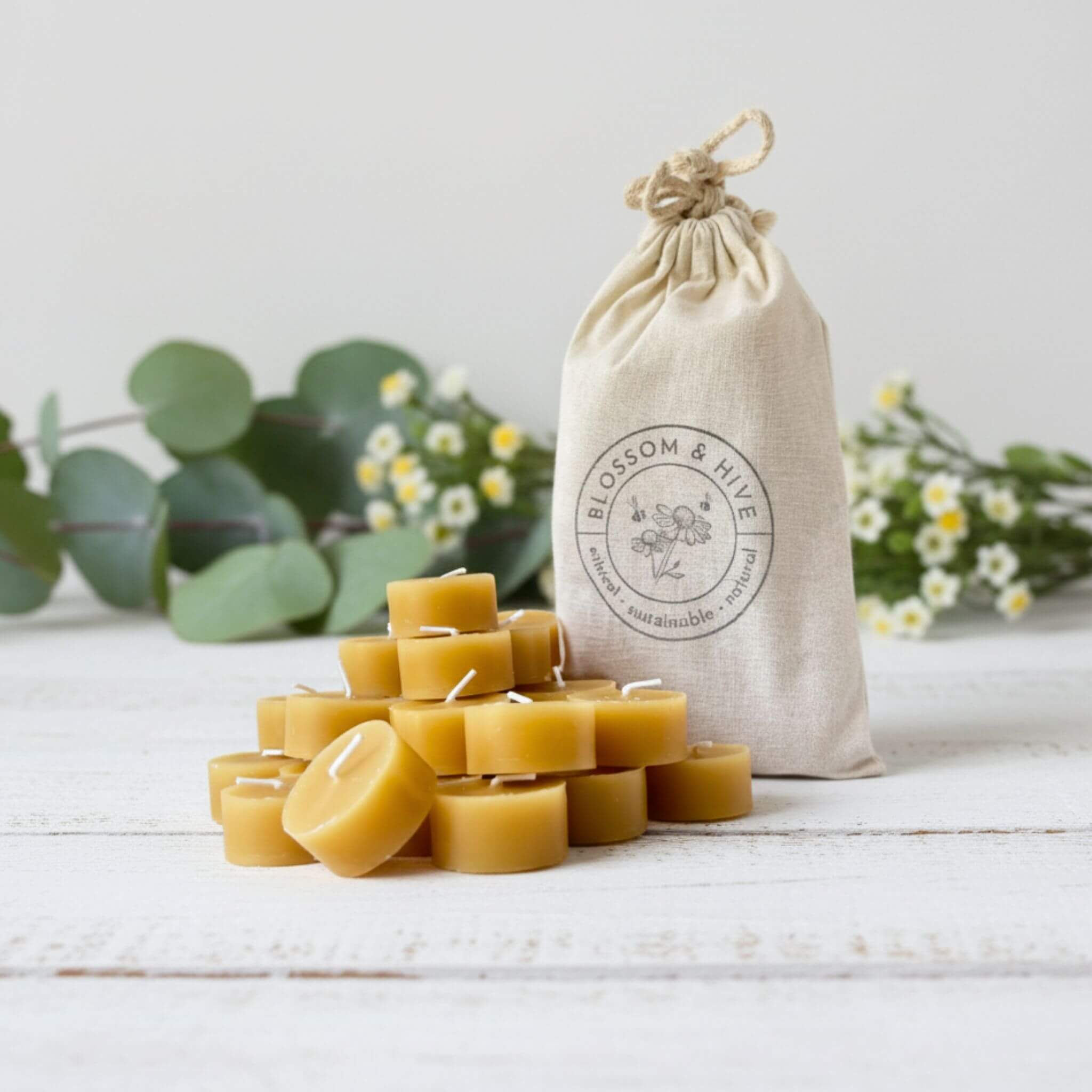 Beeswax candles stacked on a white surface with a branded cloth bag in the background.