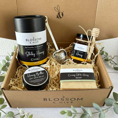 Blossom & Hive gift box with chai, tea strainer, honey, soap and balm in a gift box placed on a white timber surface with greenery around the outside