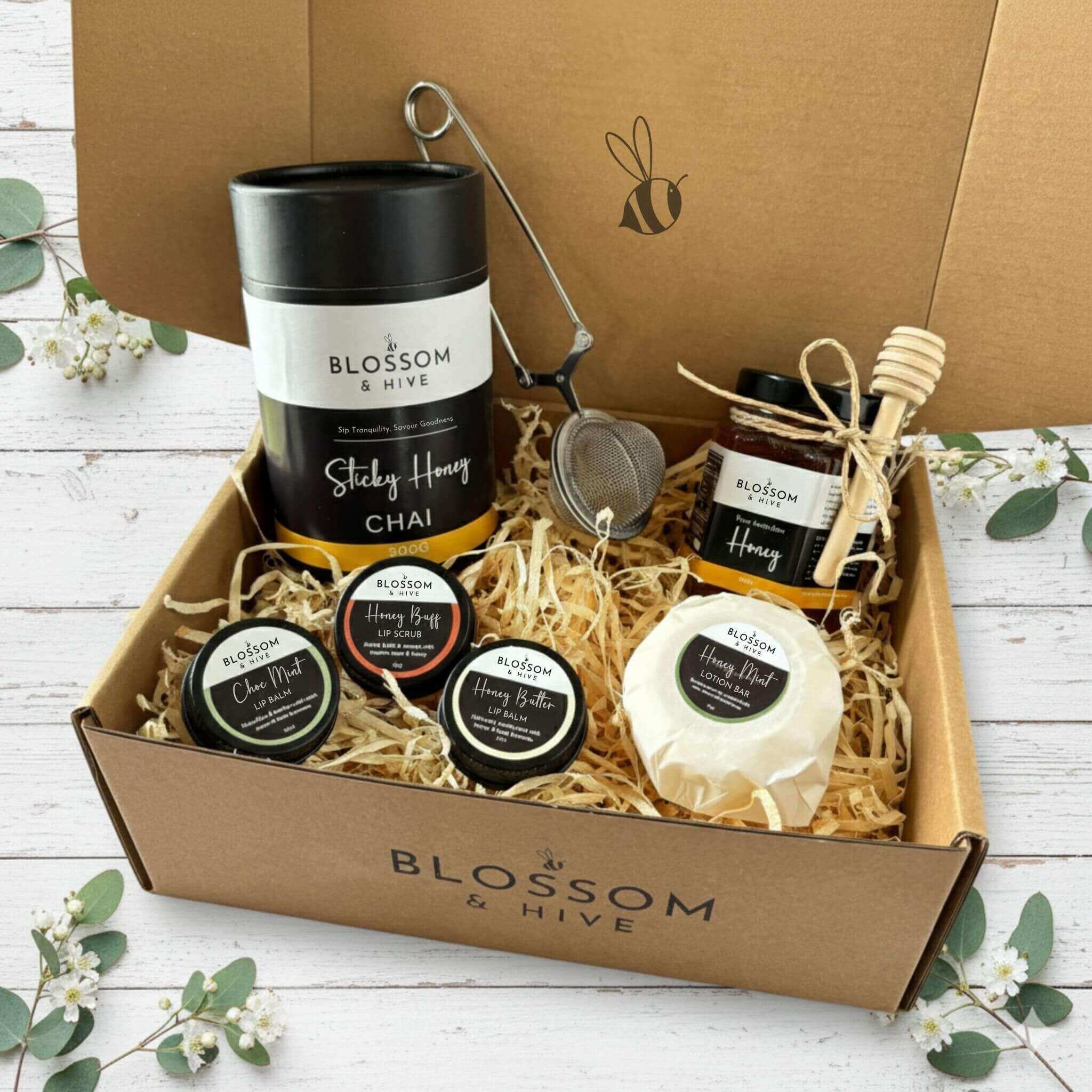 Gift box from Blossom & Hive containing honey products on a white wooden surface with greenery.