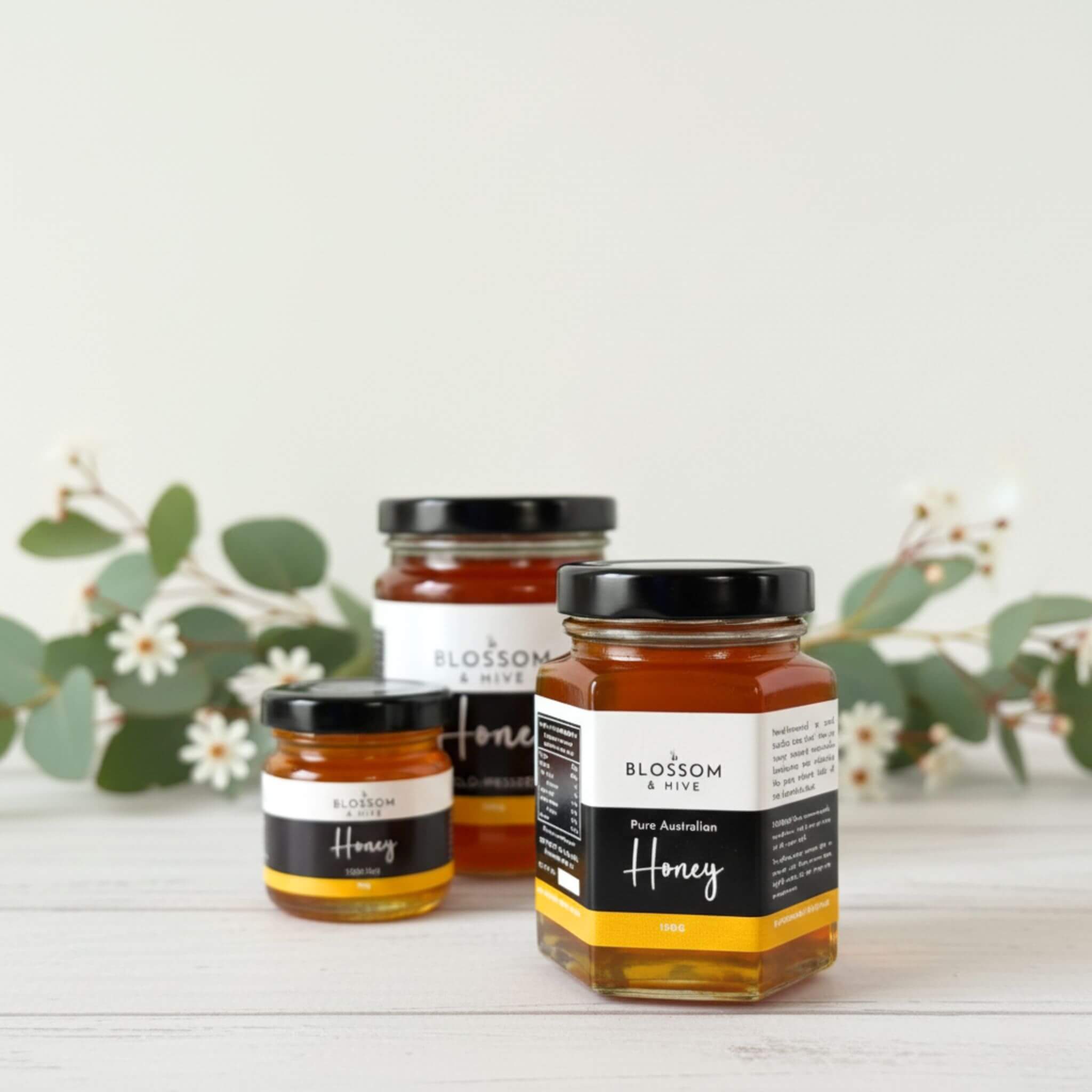 Three jars of Blossom & Hive honey on a white surface with greenery in the background