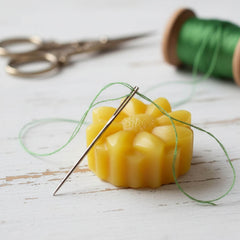 Blossom & Hive beeswax thread wax (removable) with a needle and green thread on a wooden surface