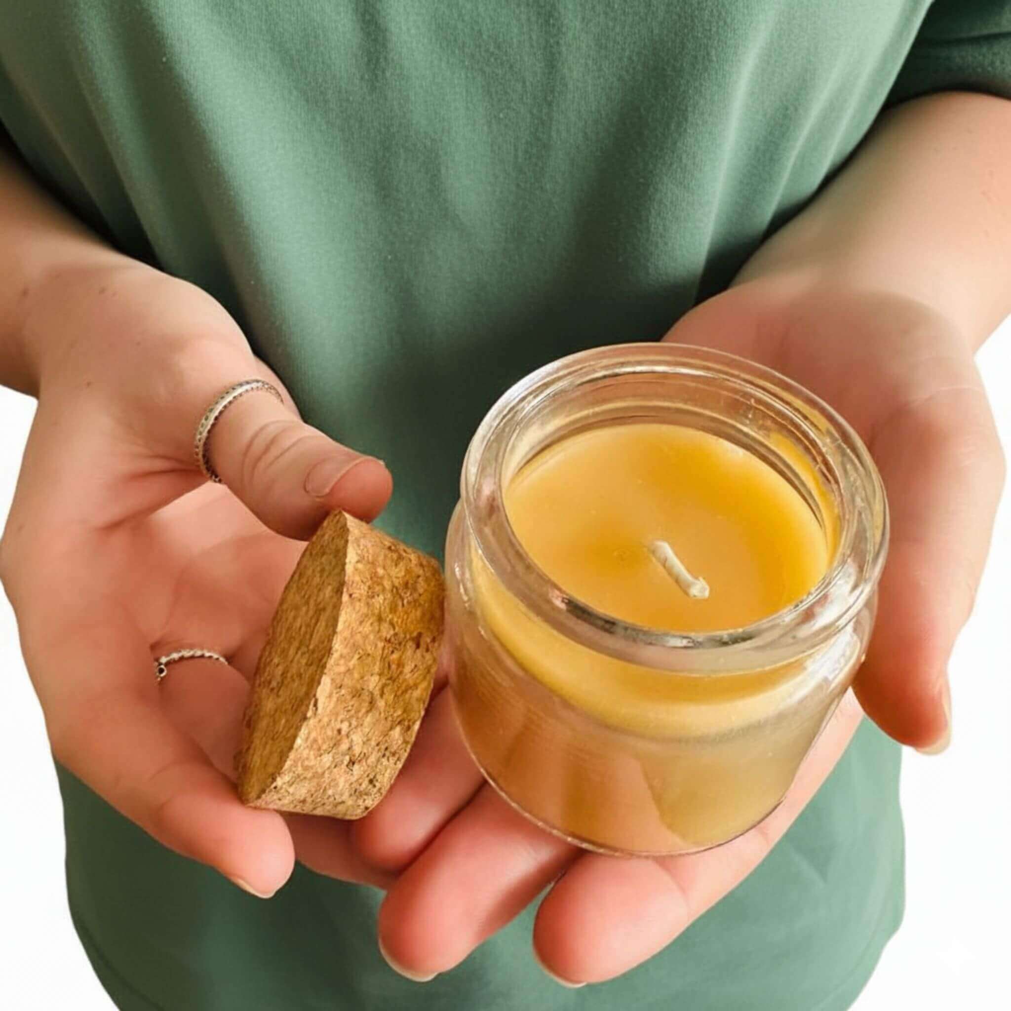 Person holding a small glass beeswax candle jar with a cork lid.
