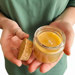 Person holding a small glass beeswax candle jar with a cork lid.