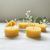 Beeswax candles on a wooden surface with a glass tealight cup in the background.