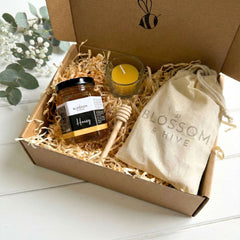 Gift box with honey, tealight candles, and a drawstring bag labeled 'Blossom & Hive' on a white surface.