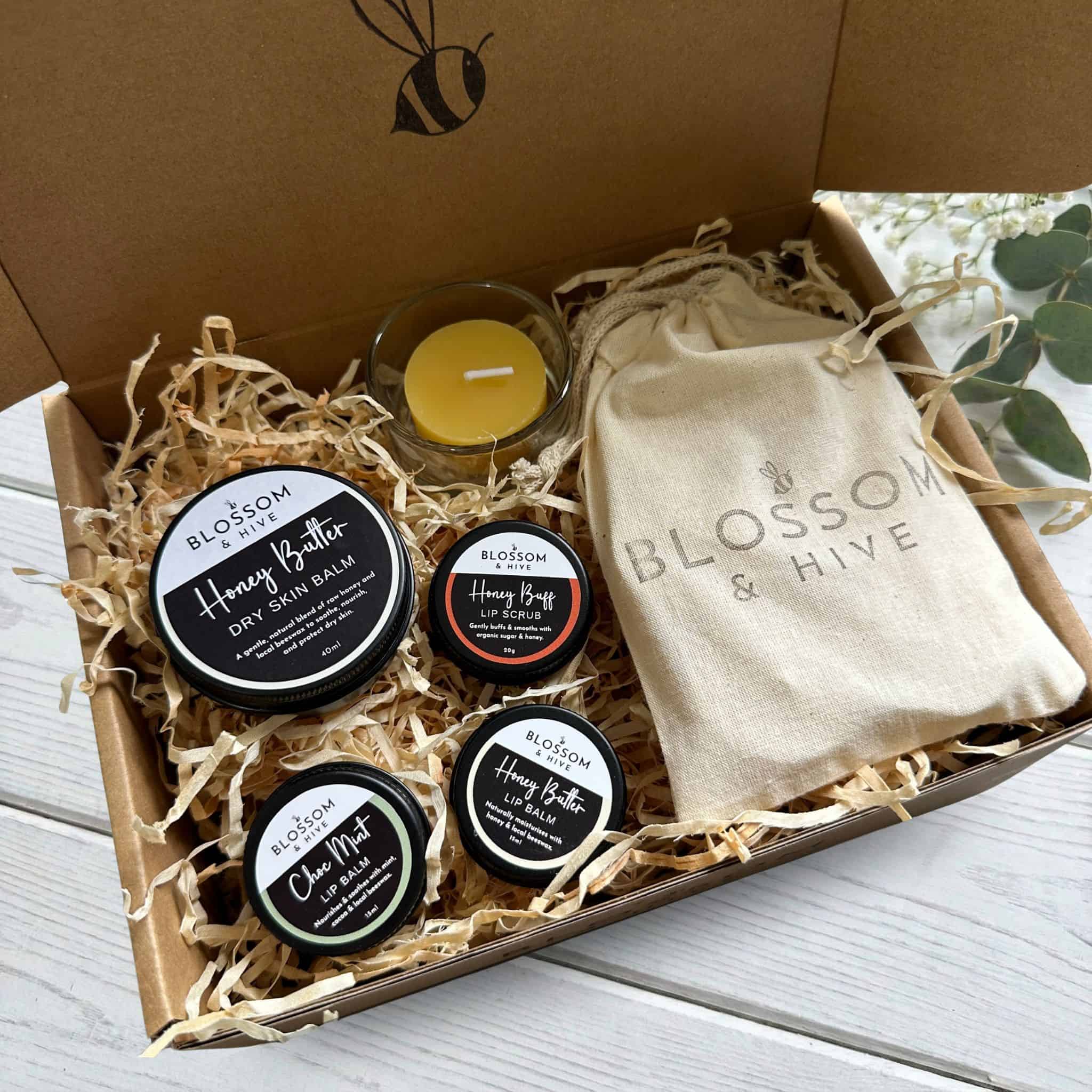 Gift box containing Honey Butter Balm, Honey Lip Care Trio, six beeswax tealight candles with a glass tealight cup, packaged in a kraft box with paper shred and a Blossom & Hive cotton bag.