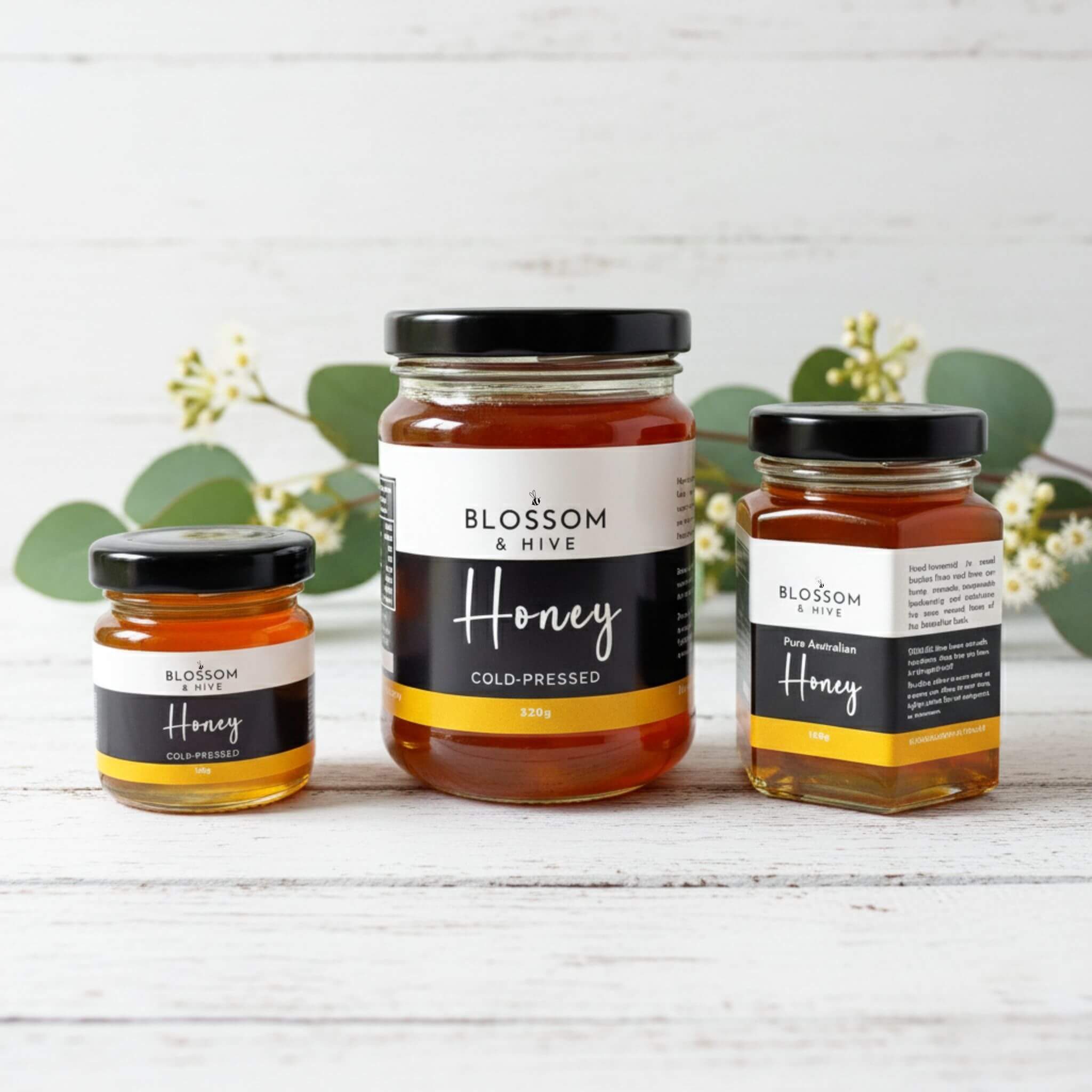Blossom & Hive local bush honey, 3 glass jars in different sizes on a white painted surface with greenery in the background
