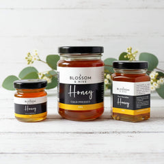 Blossom & Hive local bush honey, 3 glass jars in different sizes on a white painted surface with greenery in the background