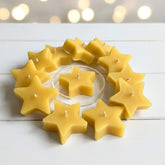 Blossom and Hive star-shaped beeswax candles arranged in a circular pattern on a white surface with blurred lights in the background.