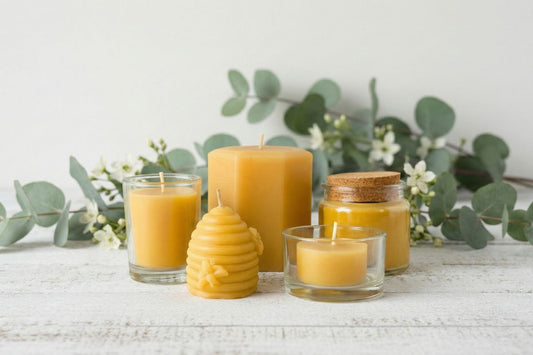 A variety of beeswax candles arranged on a white timber surface with blurred greenery behind