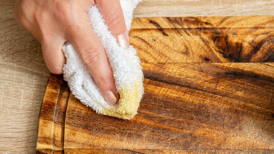 A person restoring a well-worn wooden cutting board using Collombatti Naturals' all-natural beeswax wood polish. With a soft white cloth, they gently work the polish into the wood, enhancing its rich grain and revitalising its surface.