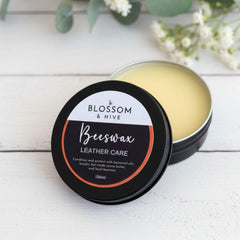 Beeswax leather care product from Blossom & Hive on a white wooden surface with greenery.