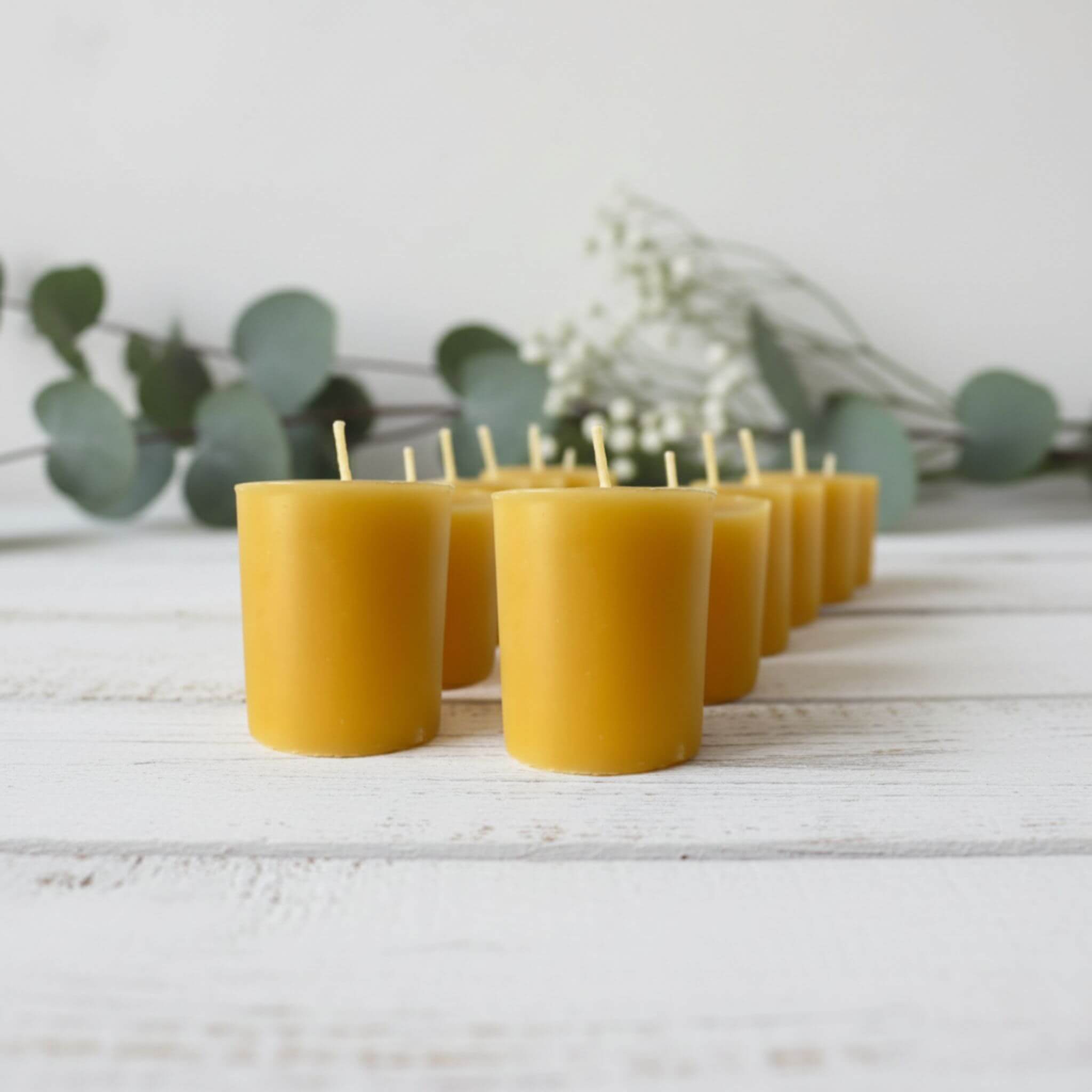 Blossom & Hive 12 beeswax votive refills lined up in a row, on a white wooden surface with greenery in the background
