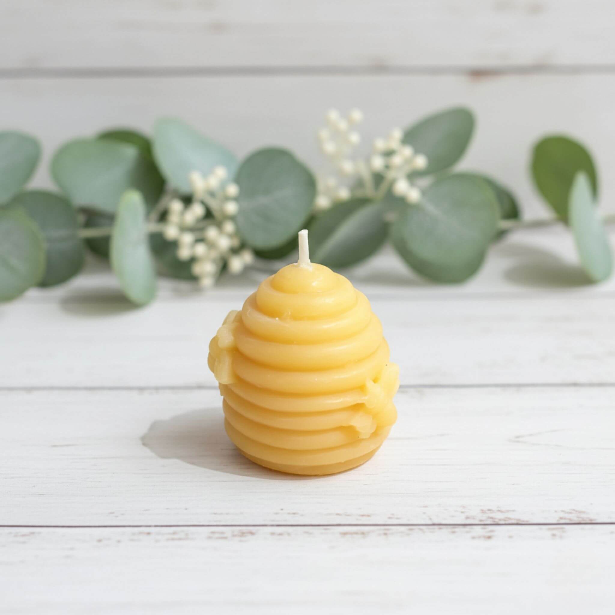 Blossom & Hive Beeswax candle shaped like a skep on a wooden surface with greenery in the background