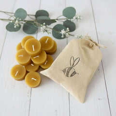 12 pack of Blossom & Hive's Beeswax candles with a drawstring bag featuring a bee design on a white wooden surface.