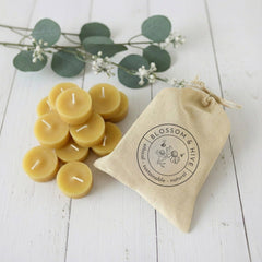 Beeswax candles with a drawstring bag labeled 'Blossom & Hive' on a light wooden surface.