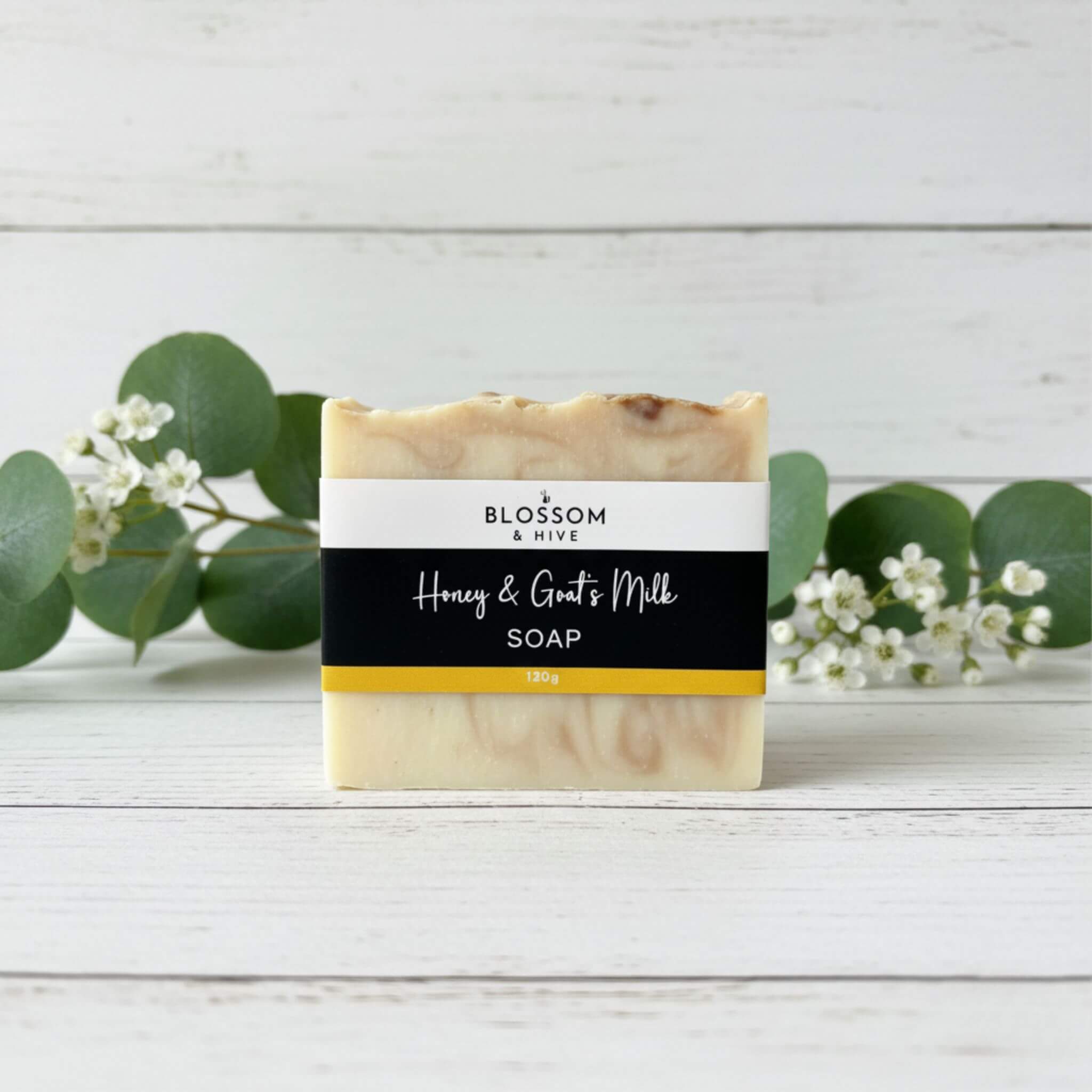Bar of Honey and Goat's milk soapon a wooden surface with greenery in the background