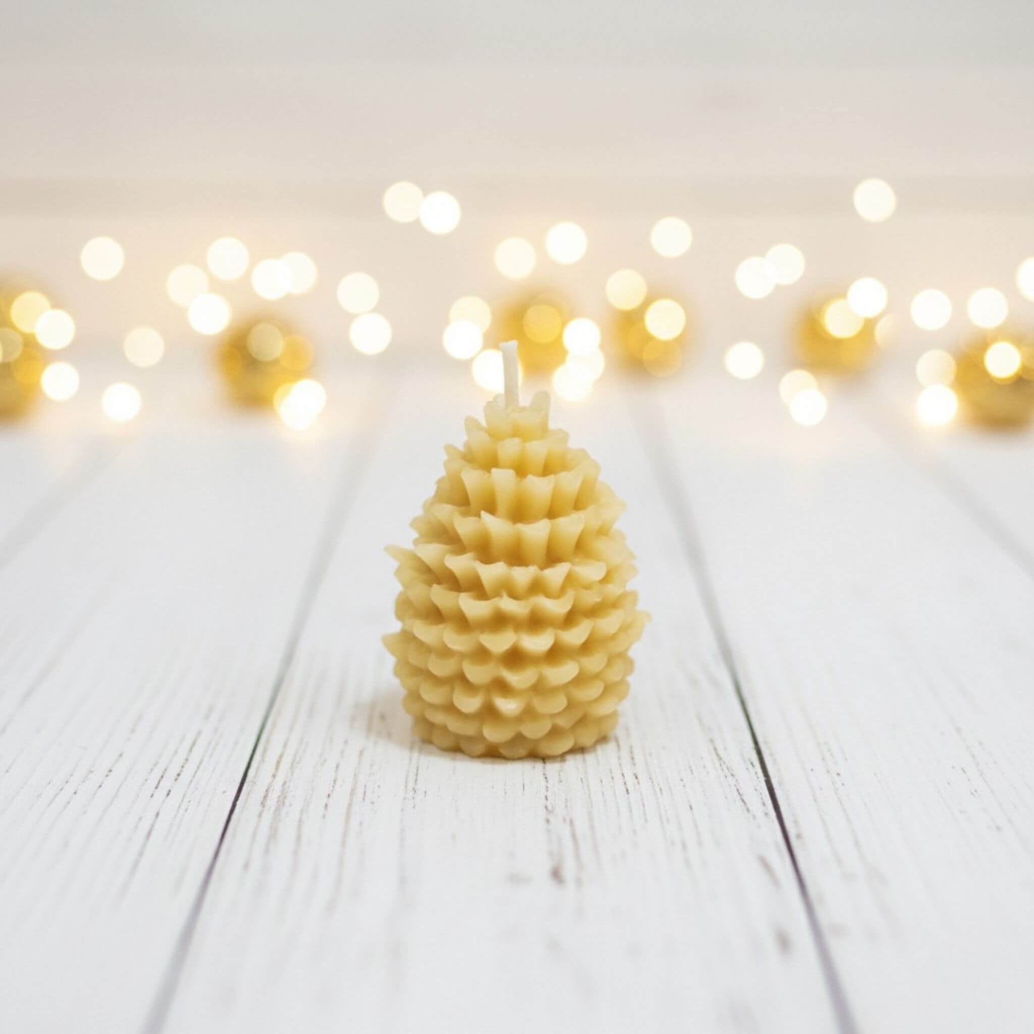 Blossom & Hive beeswax candle shaped like a pine cone on a wooden surface with blurred lights in the background