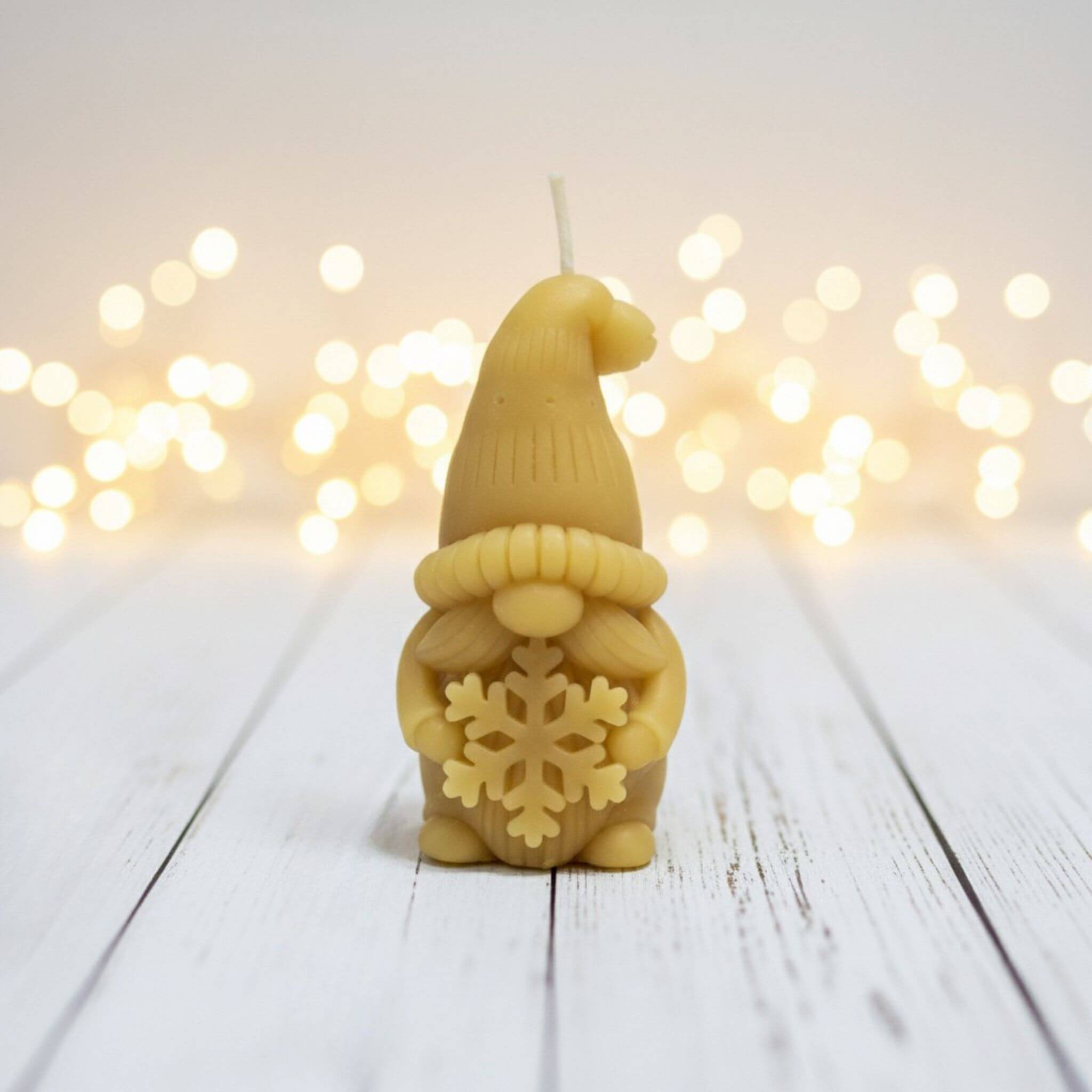 Blossom and Hive Beeswax candle shaped like a gnome with a snowflake design on a wooden surface with blurred lights in the background.