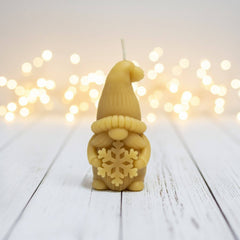 Blossom and Hive Beeswax candle shaped like a gnome with a snowflake design on a wooden surface with blurred lights in the background.