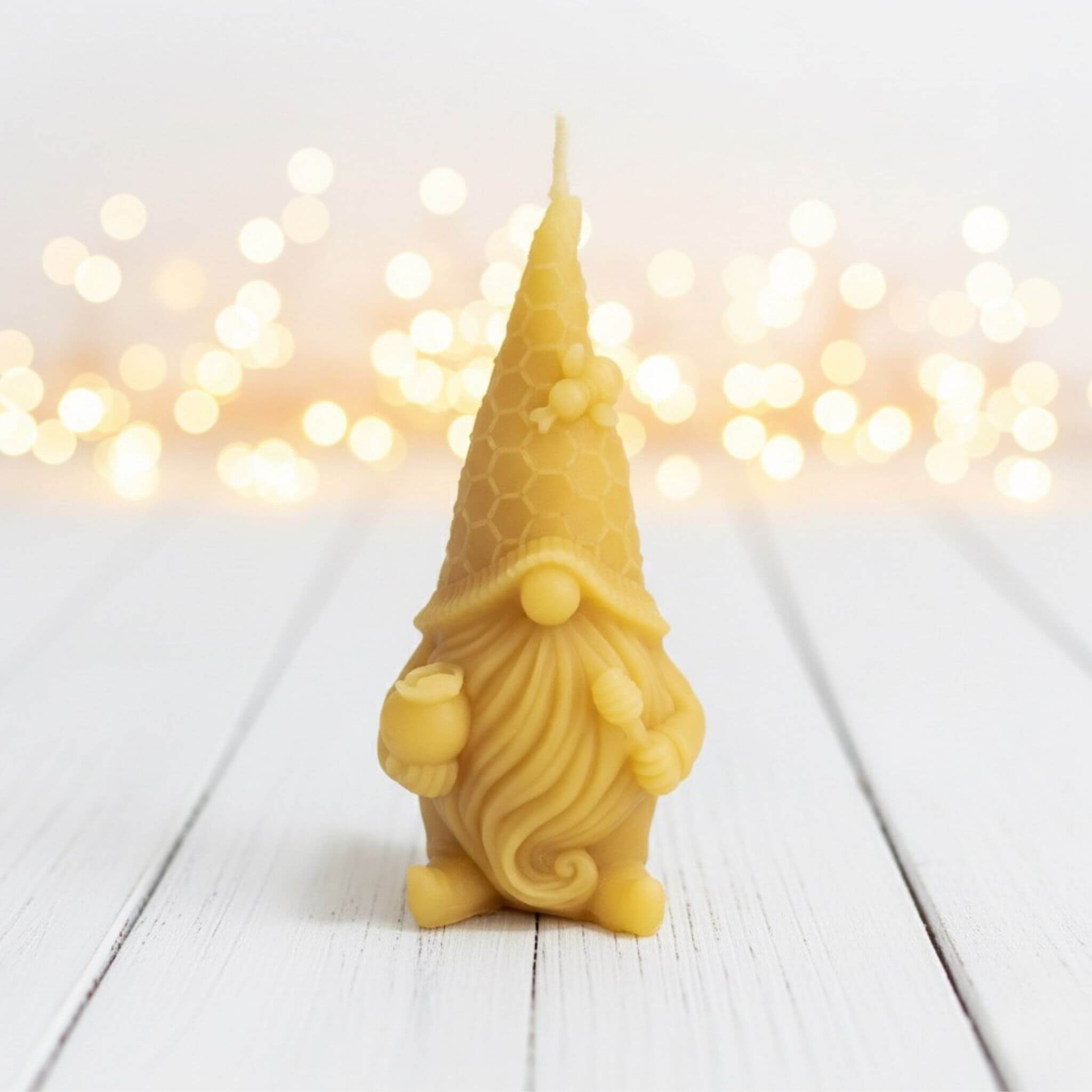 Blossom & Hive beeswax candle with gnome design on a white wooden surface with blurred lights in the background