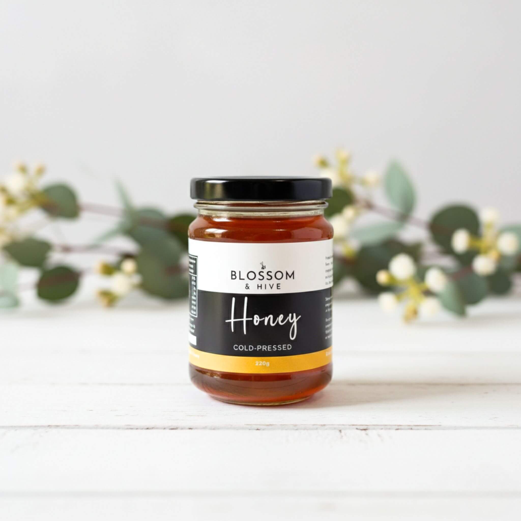 320g Jar of honey from Blossom & Hive on a white surface with greenery in the background