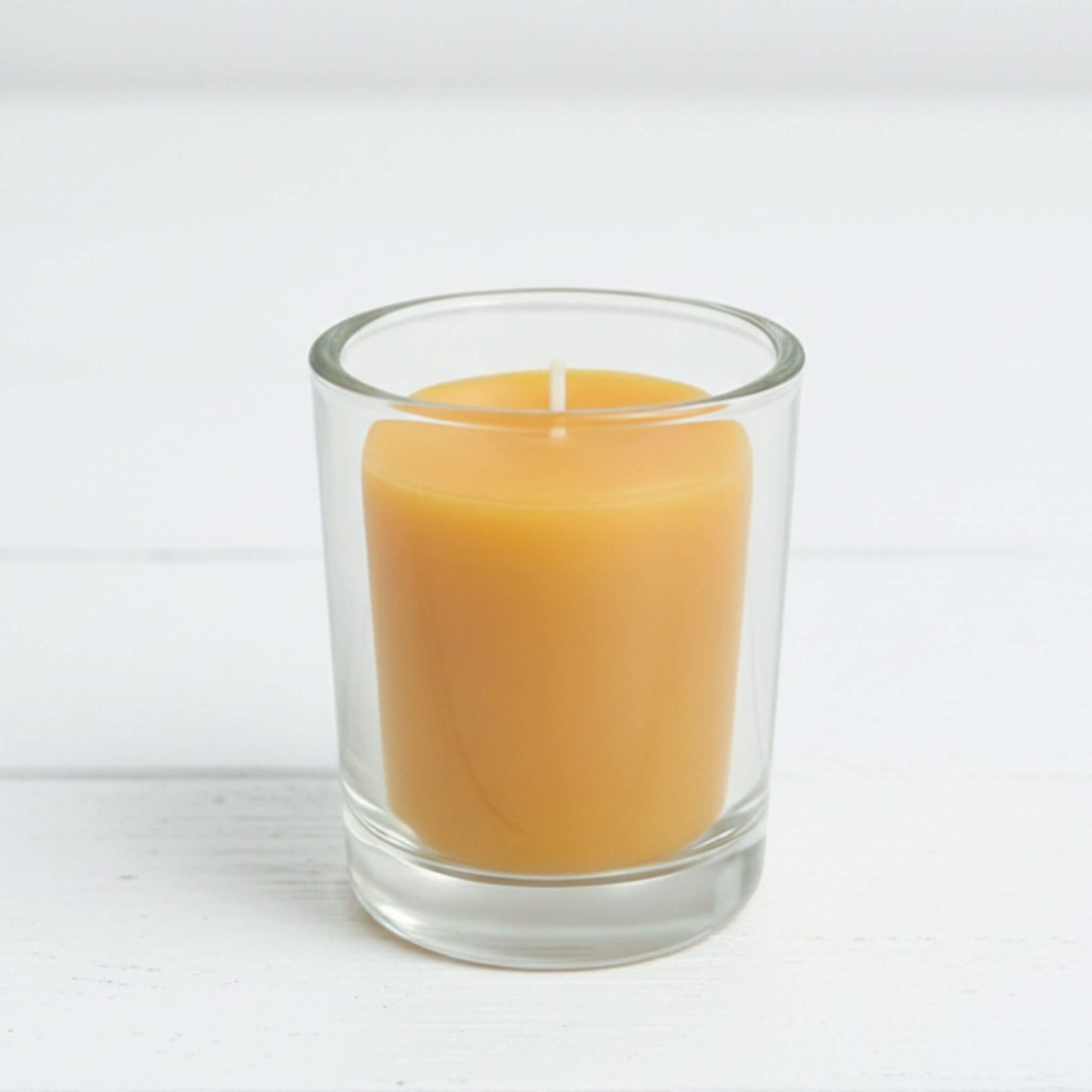 Clear glass votive candle holder with a yellow beeswax candle on a white background