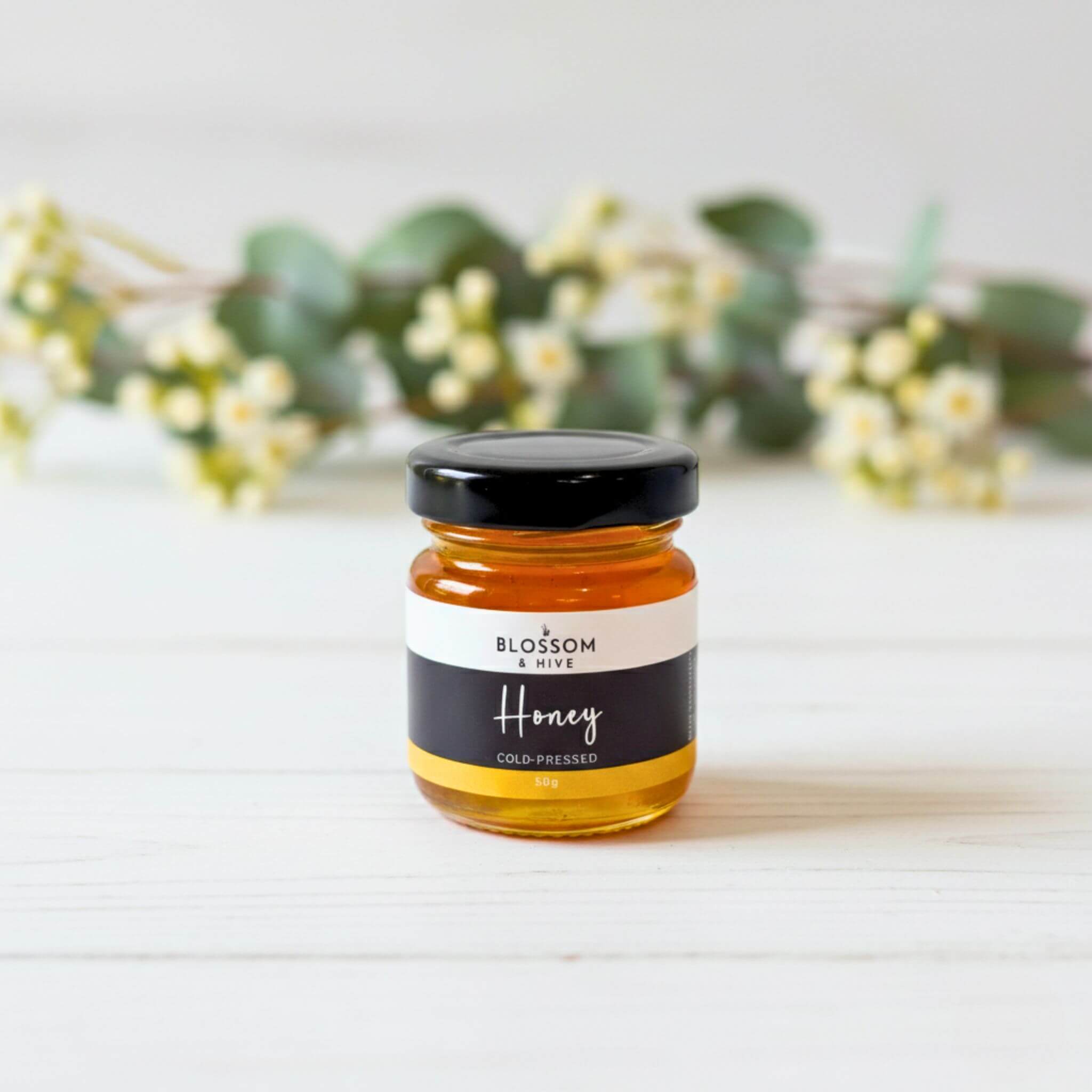 Sample size jar of Blossom and Hive local honey on a light surface with greenery in the background