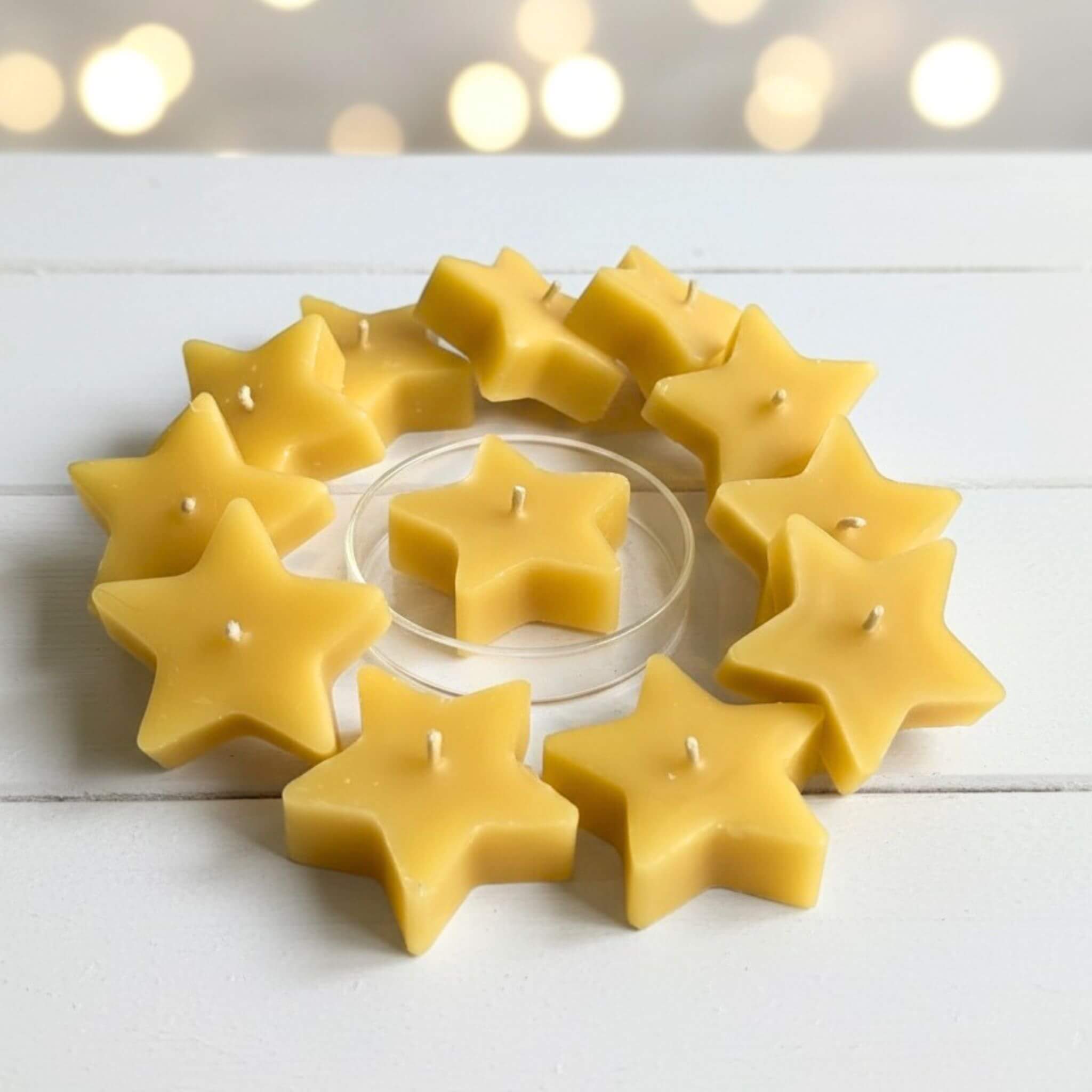 Blossom and Hive star-shaped beeswax candles arranged in a circular pattern on a white surface with blurred lights in the background.