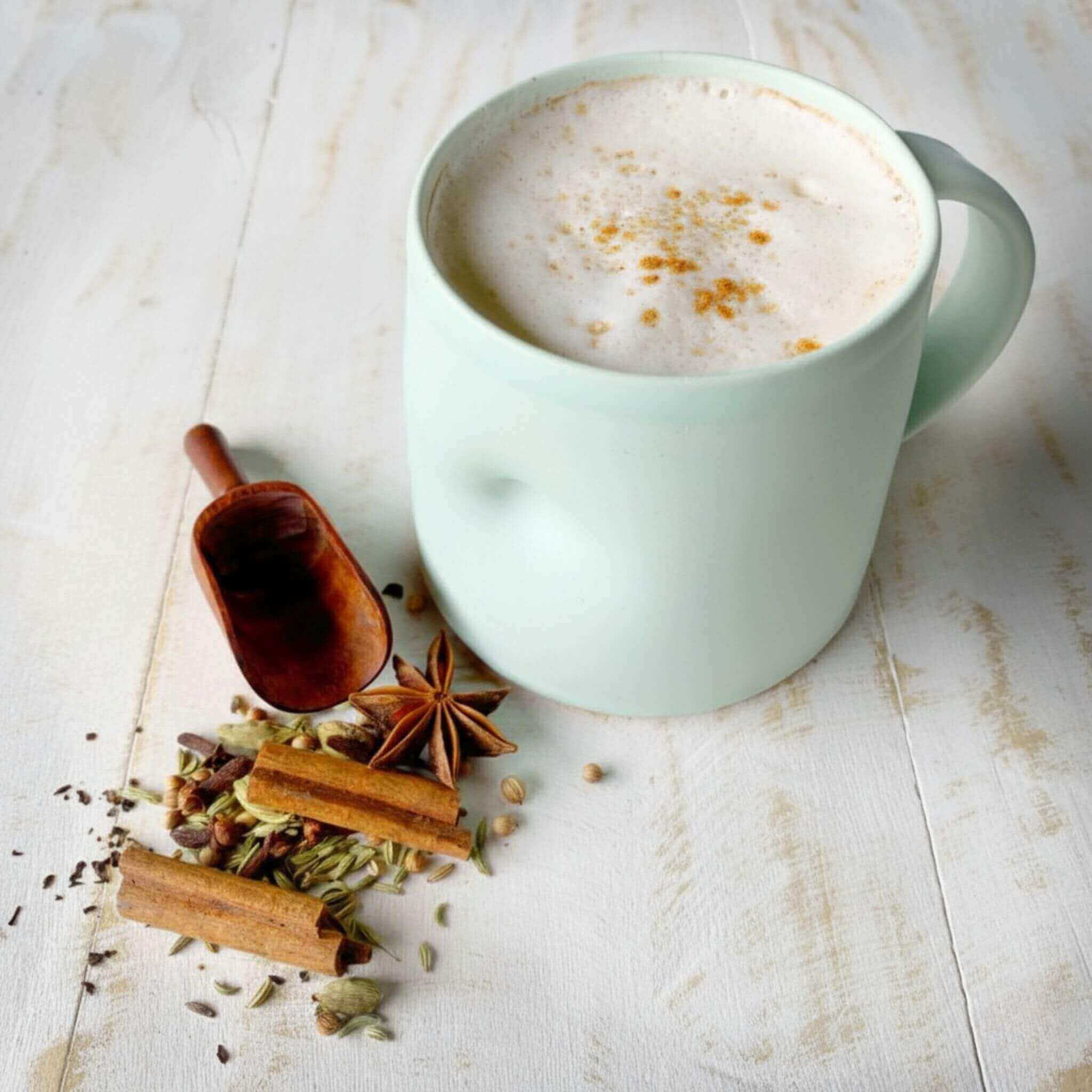 Mint green thumb mug with a Blossom and Hive sticky chai latte on a light wooden surface with spices. 