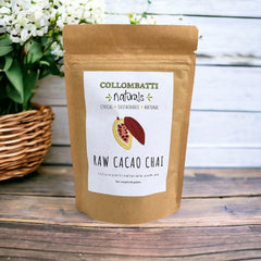 A kraft paper pouch of Collombatti Naturals Raw Cacao Chai, a rich and aromatic blend of warming chai spices and velvety raw cacao. This handcrafted, naturally sugar-free loose-leaf chai is the perfect indulgence for chai lovers seeking a smooth, chocolatey twist on a classic favourite. Set against a rustic wooden backdrop with a wicker basket and fresh flowers, evoking a sense of warmth and tradition.