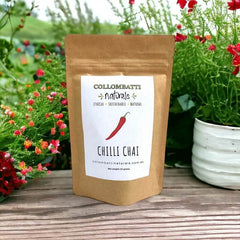 A kraft paper pouch of Collombatti Naturals Chilli Chai, featuring a bold red chilli illustration on the label. This handcrafted loose-leaf chai blends warming spices with a hint of chilli heat for a uniquely spiced and invigorating brew. Set against a vibrant garden backdrop, evoking freshness and natural goodness.