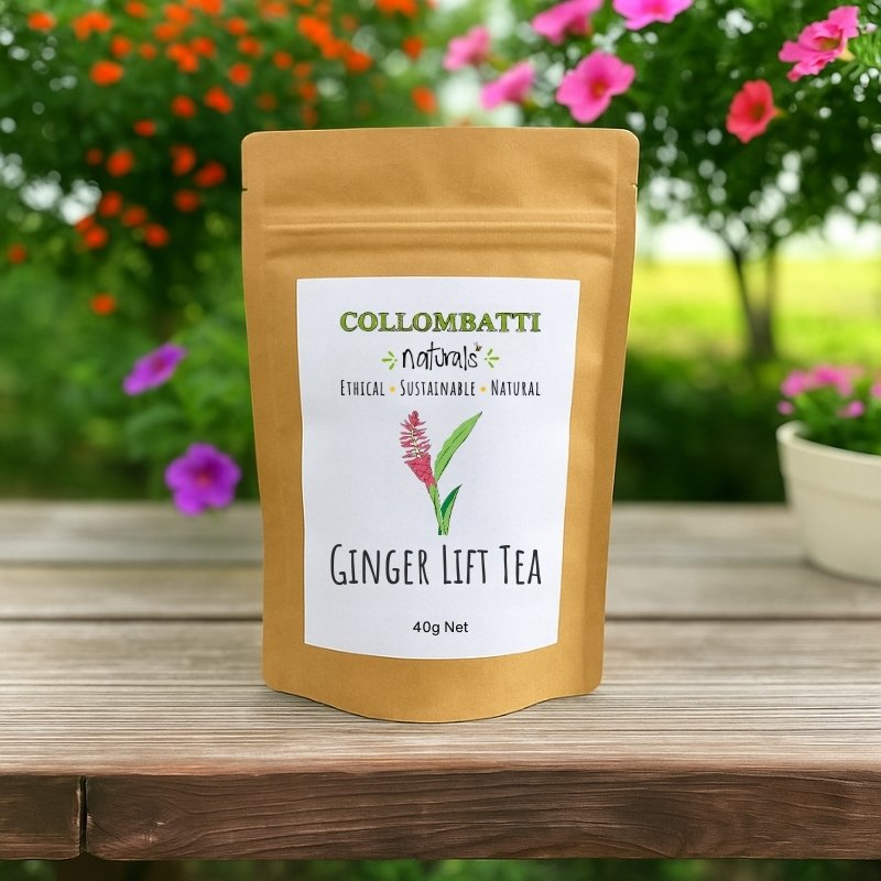 A kraft paper pouch of Collombatti Naturals Ginger Lift Herbal Tea, featuring a minimalist white label with a hand-drawn ginger plant illustration. The label highlights the brand’s ethical, sustainable, and natural values. The tea pouch is placed on a rustic wooden table with a backdrop of vibrant flowers and lush greenery, creating a fresh and uplifting aesthetic.